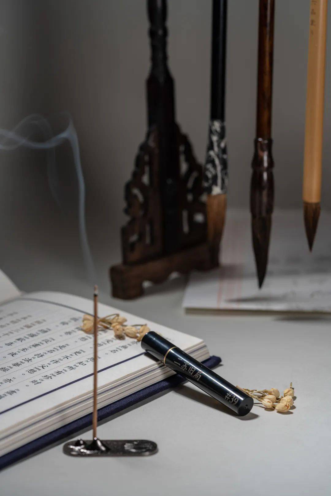 Natural incense stick burning beside a Chinese calligraphy book, with gentle smoke drifting upward—evoking mindful calm and analog stillness amid a digital world.
