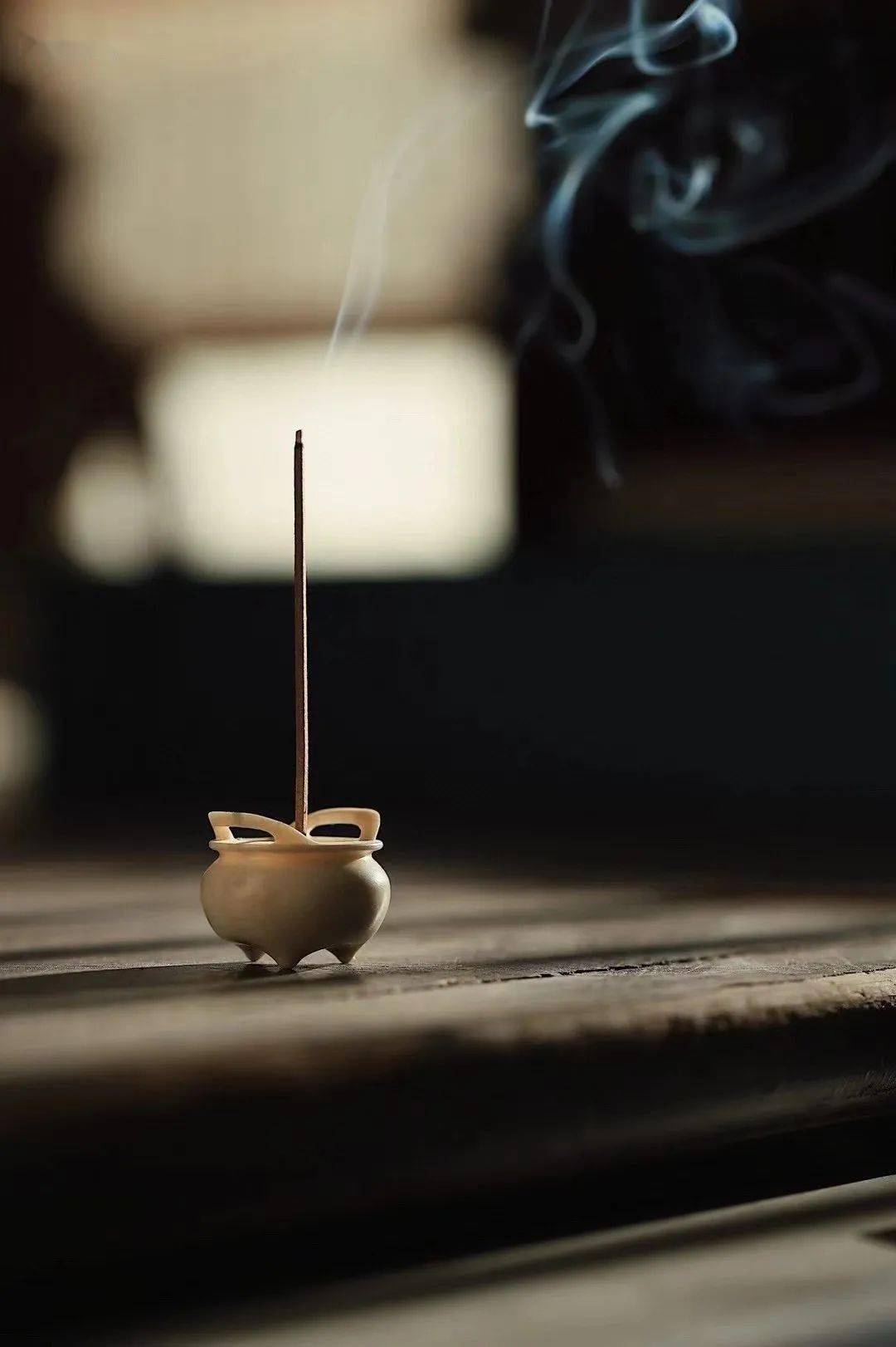 Burning incense stick with rising smoke in a ceramic holder.
