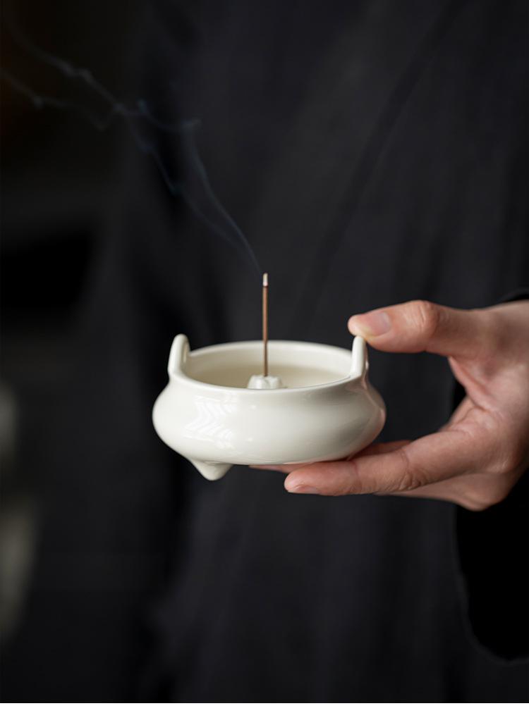 Hand holding a minimalist white ceramic Chinese incense burner with a lit natural incense stick, releasing gentle smoke — symbolizing mindfulness and Zen tranquility.