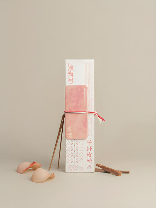 Cream-and-pink rose incense package with a pink cord, slender incense sticks and scattered rose petals.