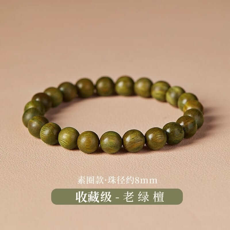 A green sandalwood bracelet with fine grain detail resting on handmade calligraphy paper, incense smoke gently drifting beside it—evoking calm, vitality, and the ancient energy of the Wood Element.