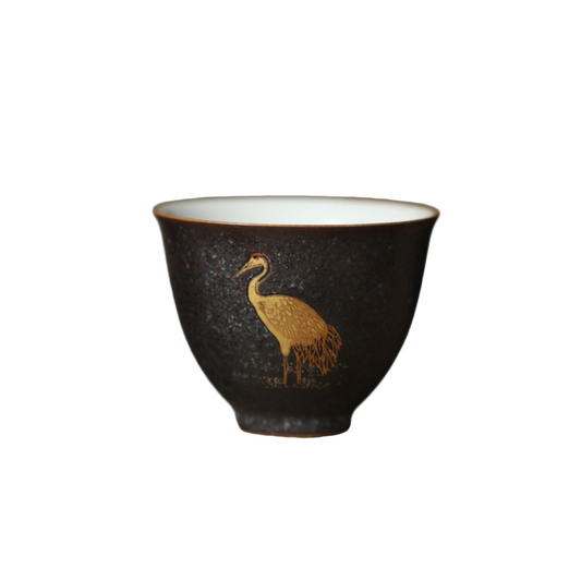 Ceramic cup with a gold bird design on a wooden surface