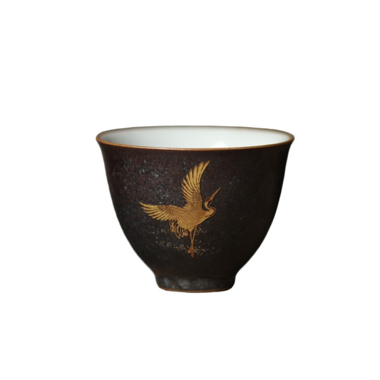 Black ceramic cup with gold bird design on a wooden surface and gray background