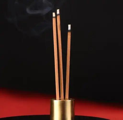 Three natural incense sticks burning in a golden incense holder against a black background.