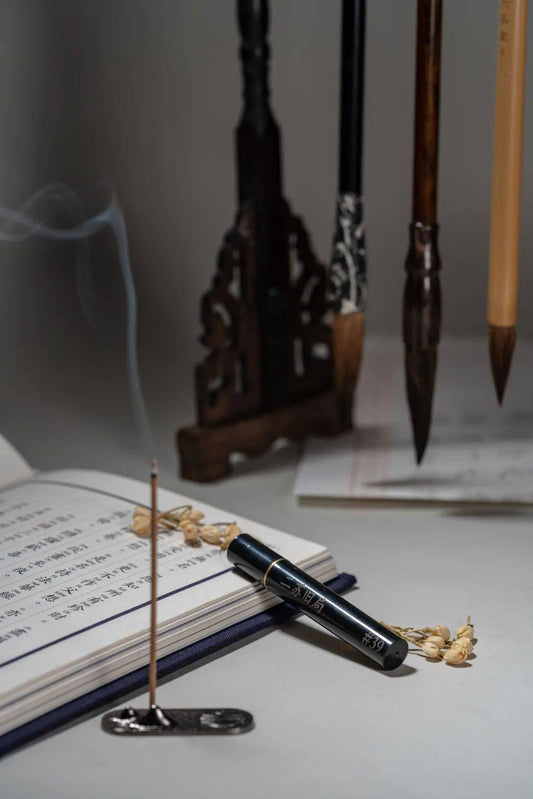 Natural incense stick burning beside a Chinese calligraphy book, with gentle smoke drifting upward—evoking mindful calm and analog stillness amid a digital world.