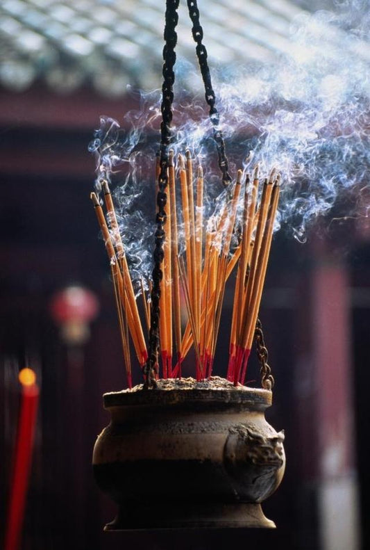 A hanging bronze incense burner filled with lit incense sticks, releasing aromatic smoke, reflecting traditional incense culture and incense history.