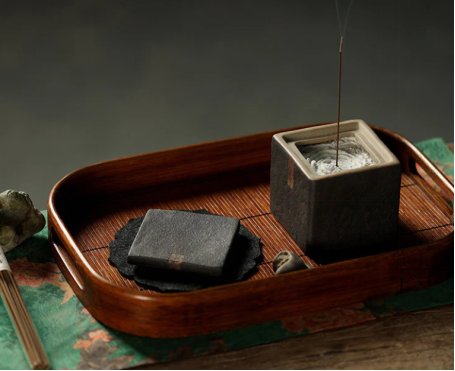 Japanese-style square ceramic incense holder with ash, arranged on a wooden tray for a minimalist, meditative setup.