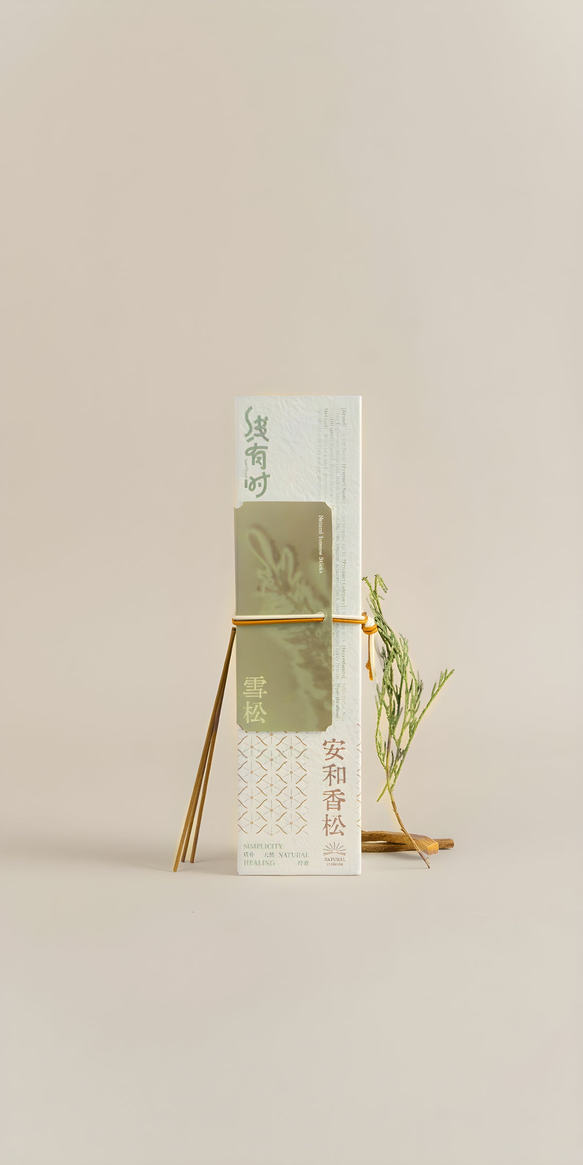 Cream-and-olive cedar incense package displayed upright on a gold stand beside a small sprig.