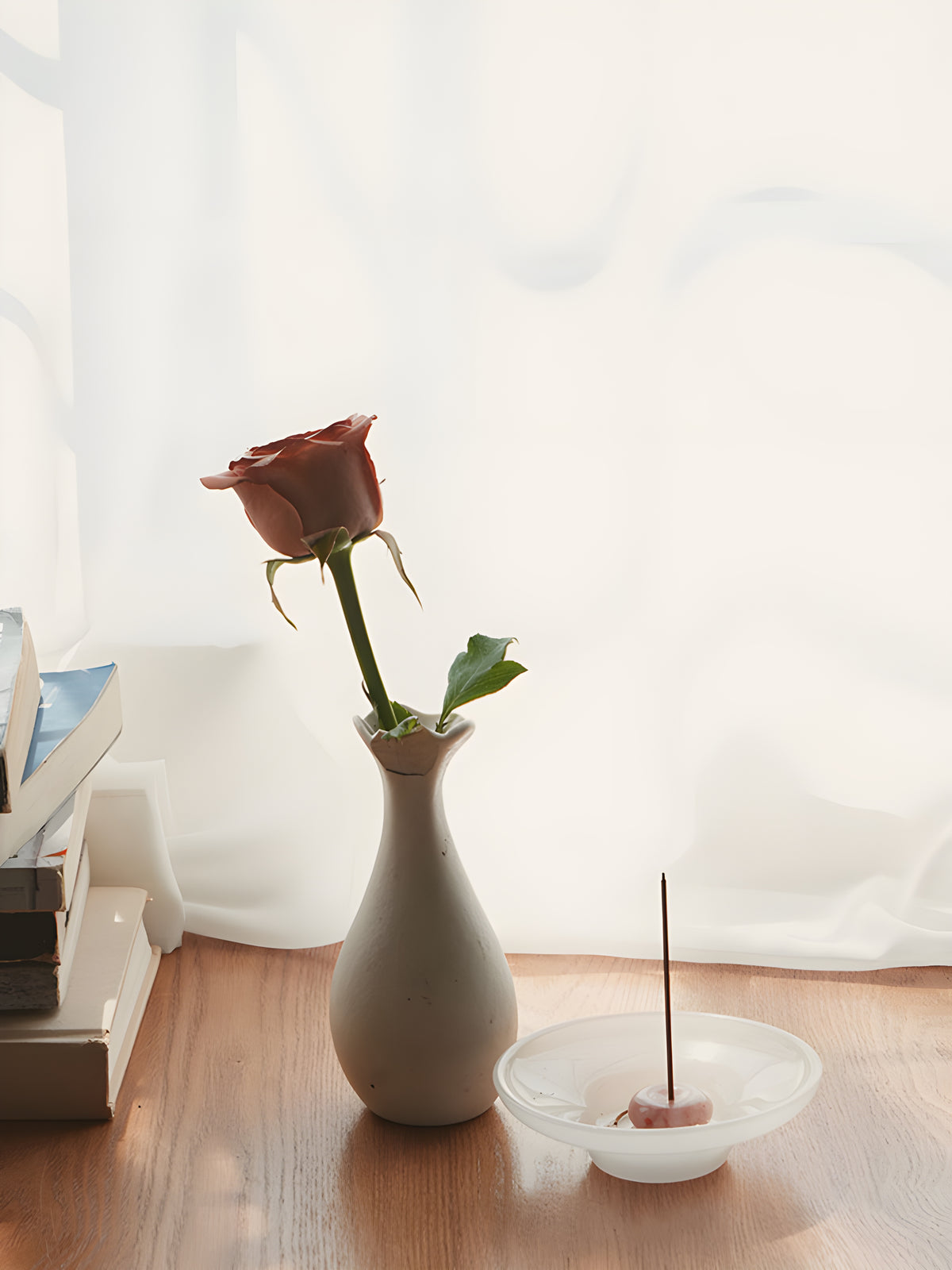 Rose incense burning in a small holder on a white dish beside a vase with a red rose.