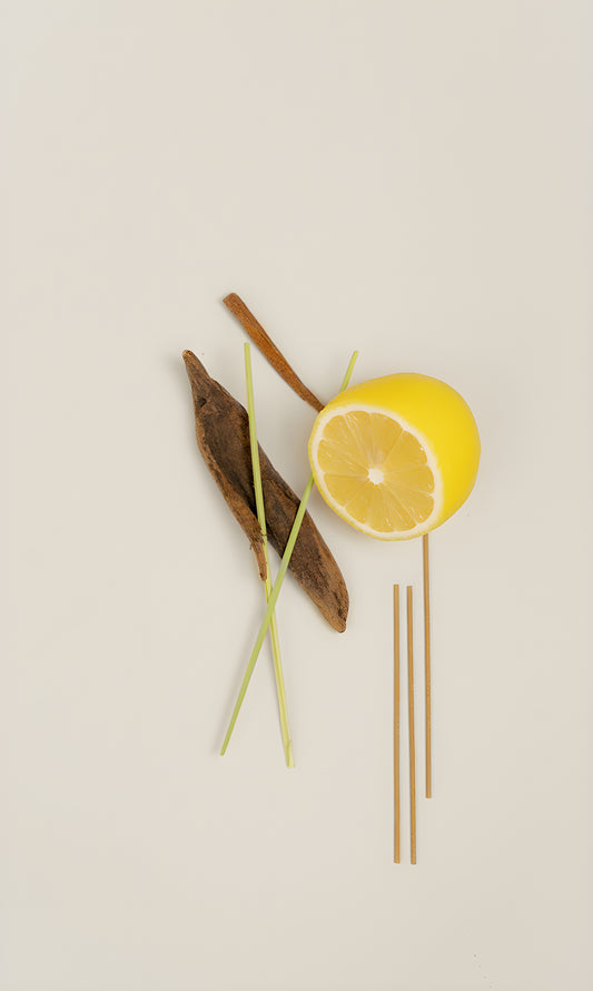 Lemongrass incense sticks arranged with a lemon half, green stems and pieces of wood.
