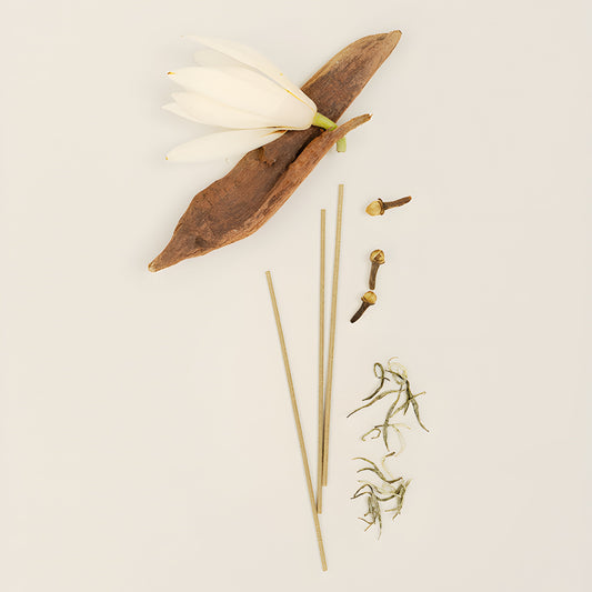 Incense sticks arranged with white flowers, green sprigs and pieces of wood on a light background.