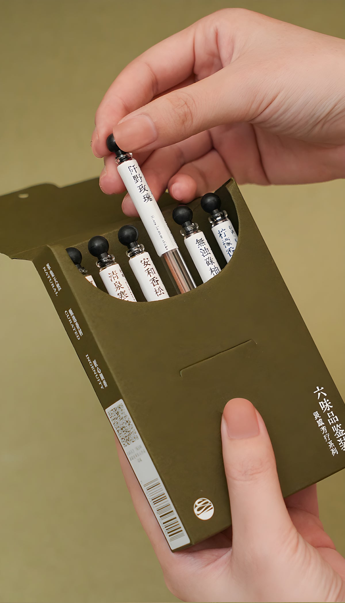 Hands lifting a labeled incense sample tube from the six-fragrance discovery box.