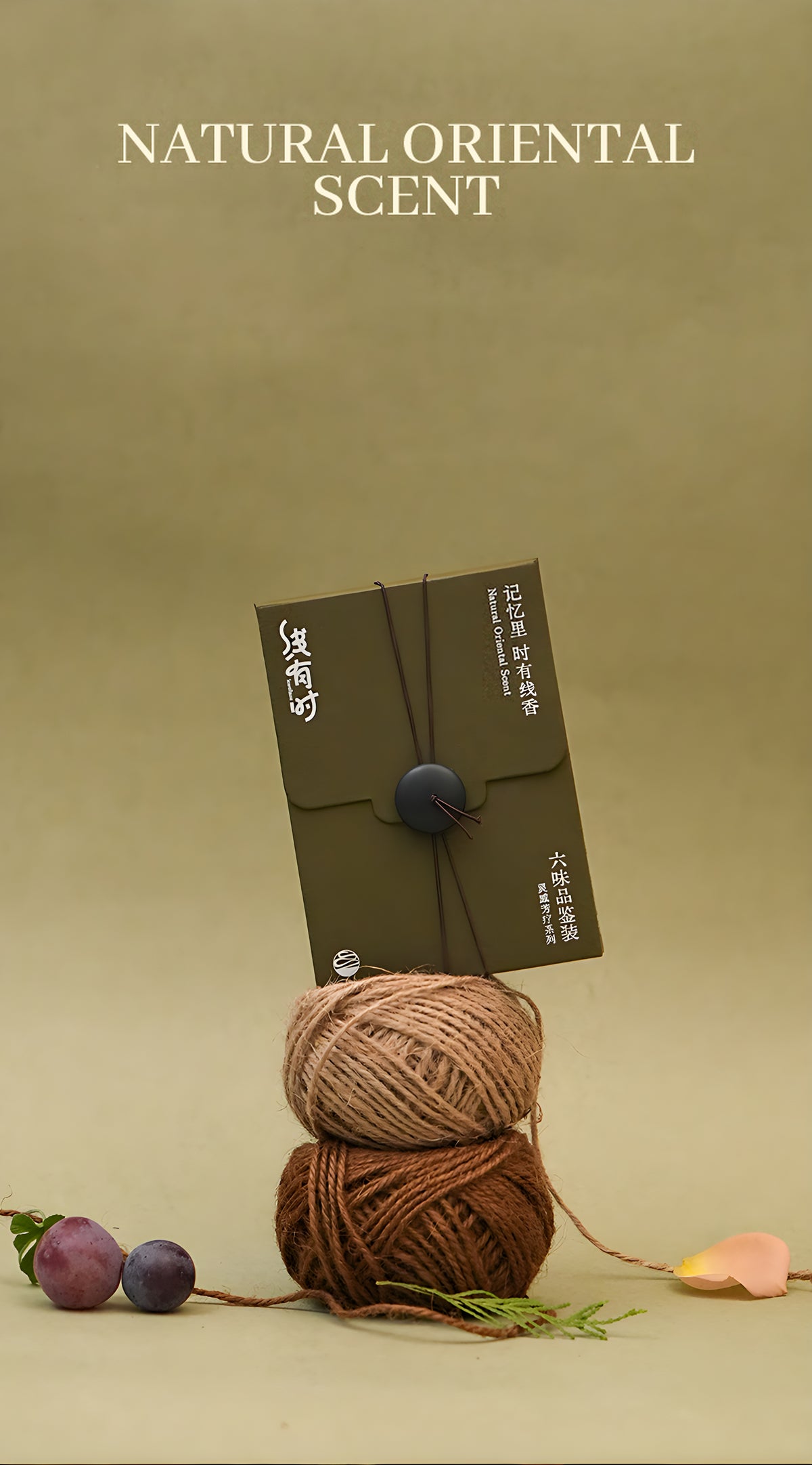 Closed olive-green incense discovery box styled on a twine ball with grapes and rose petals.