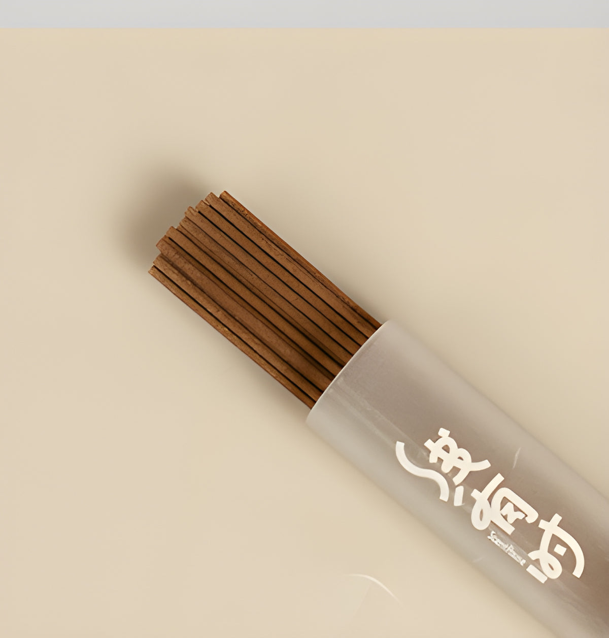 Close-up of slender brown cedar incense sticks extending from a frosted storage tube.