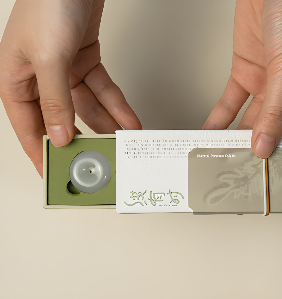 Hands sliding open the cedar incense box to reveal the olive-green tray and round holder.