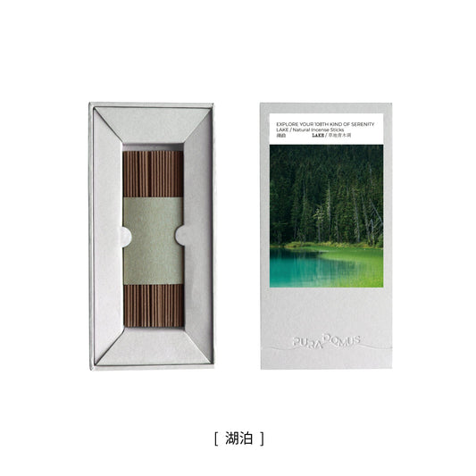 A lit incense stick resting in a silver paper holder beside a kraft box, surrounded by soft morning light and misty hues—evoking the stillness of a mountain lake and the inward flow of the Water Element.

