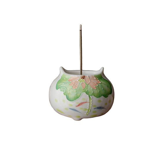 Ceramic incense holder with floral design held by a person against a dark background