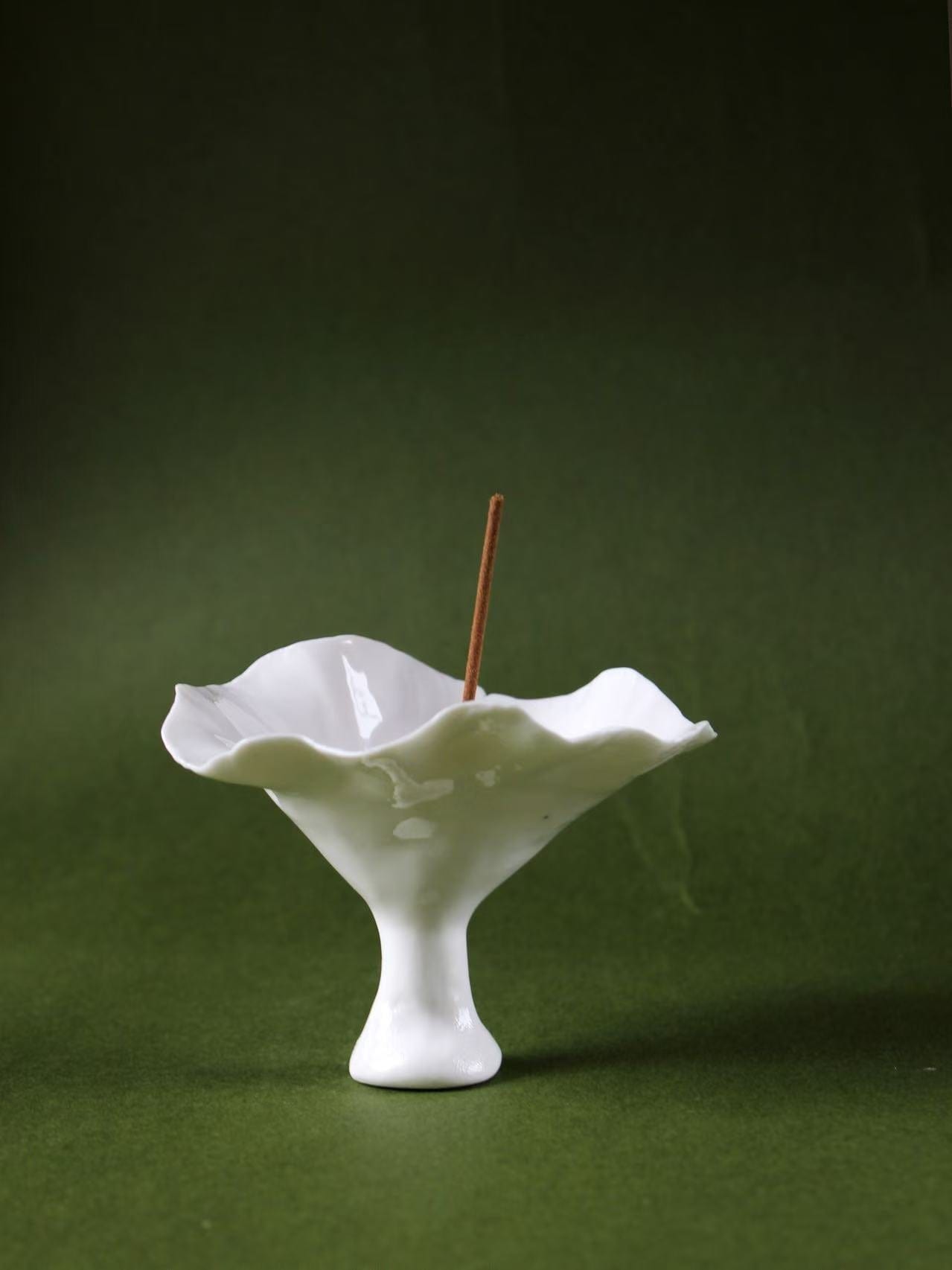 A handmade ceramic incense holder shaped like an open flower, holding a lit stick of incense—evoking natural grace, upward energy, and meditative stillness.