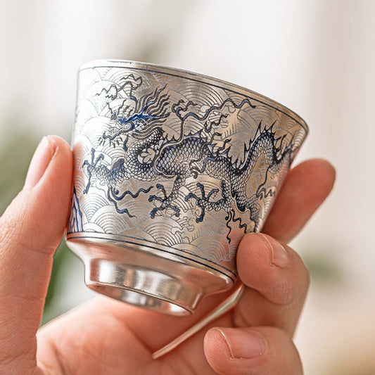 Hand holding a silver cup with dragon engraving against a blurred background