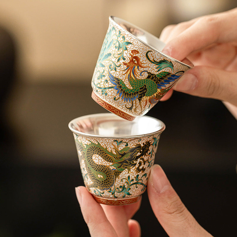 Hand holding a pair of dragon and phoenix cloisonné silver-lined Chinese teacups