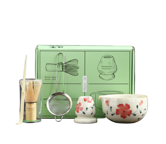 Tea-making set with a green box, whisk, strainer, small cup, and decorative bowl on a wooden surface.