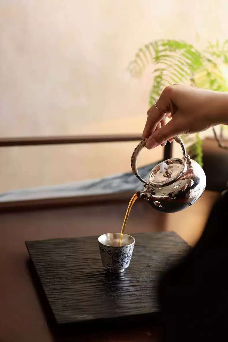Tea being poured from a teapot into a cup on a wooden table.