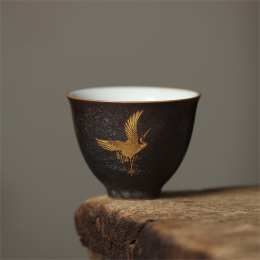 Black ceramic cup with gold bird design on a wooden surface and gray background